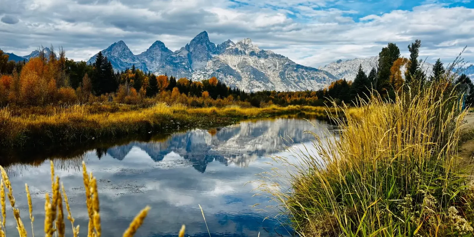 Grand Teton mountains reflected in water beneath an autumn sky